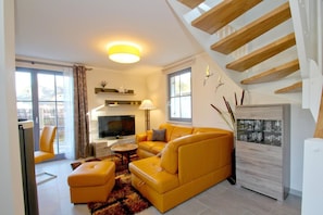 A modern living room with a yellow sofa, a flat-screen TV, a fireplace, and a staircase. - Vacation home Stranddistel - close to the beach, thatched roof, with garden, sauna, dog-friendly (Glowe)