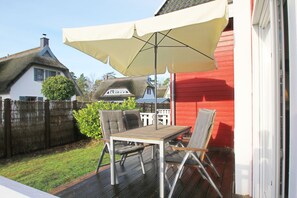 Une terrasse avec une table et des chaises, un grand parasol et, au fond, un bâtiment rouge.