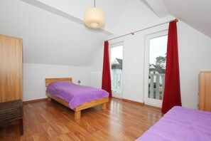 Une chambre avec un lit en bois, un rideau rouge, une armoire en bois et une vue sur une maison, visible à travers une porte coulissante.