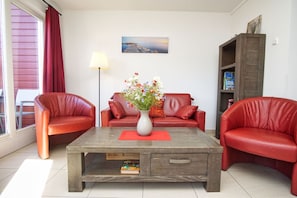 Ein Wohnzimmer mit Couchtisch aus Holz, roten Ledersofas, einer Blumenvase, einer Lampe und einem Bücherregal.