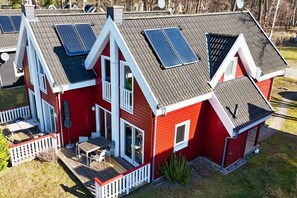 Ein rotes Haus mit Solaranlage auf dem Dach, einer Terrasse und einem kleinen Garten.