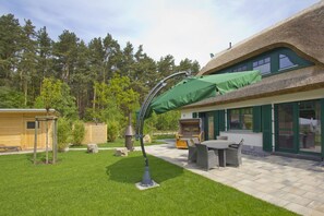 Un jardín cuidado con un patio, mobiliario exterior y un edificio con techo de paja.