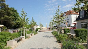 A paved pathway with benches, surrounded by greenery and buildings. - Ferienhaus Seehund - House in a great location with garden, terrace and private sauna (Glowe)