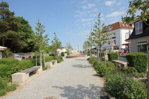 A paved pathway with benches, surrounded by greenery and buildings. - Ferienhaus Seehund - House in a great location with garden, terrace and private sauna (Glowe)