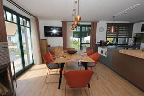 Una cocina moderna con comedor, que cuenta con una mesa grande, sillas anaranjadas y un televisor montado en la pared.