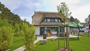 A thatched-roof building with a patio area, outdoor seating, and a swing set. - Ferienhaus Seehund - House in a great location with garden, terrace and private sauna (Glowe)
