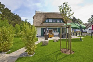 A thatched-roof building with a patio area, outdoor seating, and a swing set. - Ferienhaus Seehund - House in a great location with garden, terrace and private sauna (Glowe)