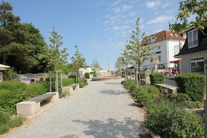 Un chemin pavé, bordé de bancs, entouré de verdure et de bâtiments.