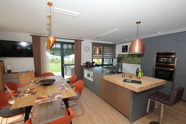 A modern kitchen with a central island, pendant lighting, and a dining area with orange chairs.