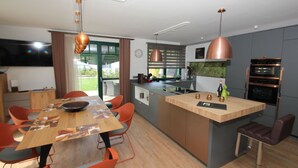 A modern kitchen with a central island, pendant lighting, and a dining area with orange chairs. - Ferienhaus Seehund - House in a great location with garden, terrace and private sauna (Glowe)