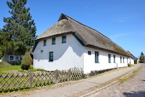 Ein traditionelles weißes Gebäude mit einem Reetdach, einem Holzzaun und einem gepflasterten Weg.