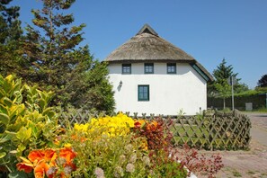 Ein weißes Haus mit Strohdach, umgeben von einem Holzzaun und bunten Blumen.