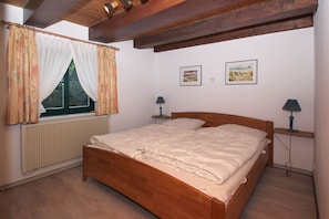 A bedroom with a wooden bed, a window with curtains, two bedside lamps, and two framed pictures on the wall. - Waterfront house with terrace and garden - Ferienhaus Storchennest Haus L - (Wiek)