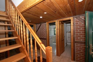 Eine Holztreppe führt zu einer unteren Ebene mit einer Ziegelwand und einer Glastür.
