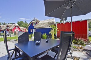 An outdoor patio with a table and chairs, a large umbrella, and a red shed in the background. - Haus Ostseesonne - close to the beach, quiet location, own sauna, beautiful garden - (Glowe)