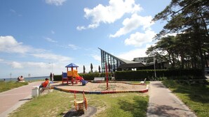 Ein Spielplatz mit Rutschen und Schaukeln, ein gepflasterter Weg und ein Gebäude im Hintergrund.