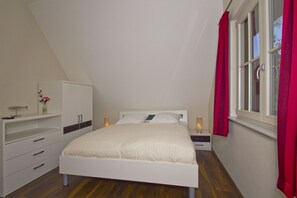 A bedroom with a bed, a wardrobe, a nightstand, and a window with curtains. - Haus Ostseesonne - close to the beach, quiet location, own sauna, beautiful garden - (Glowe)