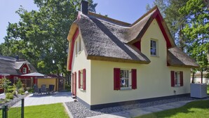 Ein traditionelles Haus mit einem steilen Satteldach, roten Fensterläden und einem gepflegten Garten.