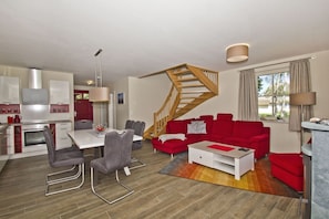 A modern living space with a dining area, red sofa, staircase, and kitchen. - Haus Ostseesonne—close to the beach, quiet location, private sauna, beautiful garden— (Glowe)