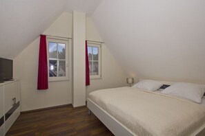 A bedroom with a bed, two windows, a TV, and a wardrobe. - Haus Ostseesonne—close to the beach, quiet location, private sauna, beautiful garden— (Glowe)