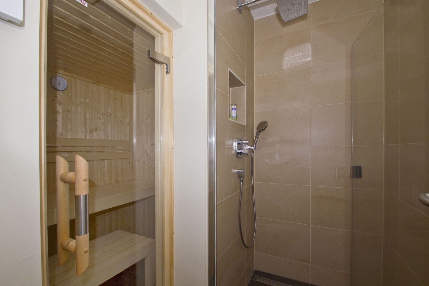 A wooden sauna with a bench and a shower area with tiled walls and a handheld showerhead.
