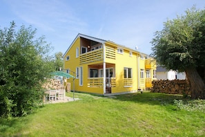 Ein gelbes, zweistöckiges Haus mit Balkon, Steinmauer und grünem Sonnenschirm.