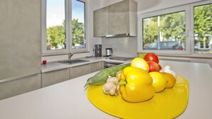 A modern kitchen with large windows, a white countertop, and a variety of fresh fruits and vegetables. - Vacation home Saga - close to the beach, modern house with own sauna, garden, terrace - (Wiek)