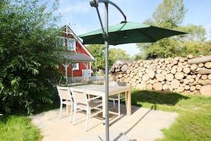 Eine Terrasse im Freien mit Tisch und Stühlen, einem grünen Sonnenschirm und einem roten Gebäude im Hintergrund.