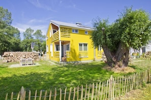 A yellow two-story house with a front porch, a wooden fence, and a large tree in the yard.