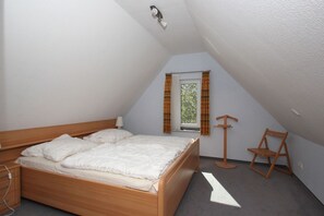 Une chambre avec un lit en bois, une fenêtre avec des rideaux, une chaise en bois et une petite table.