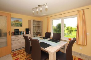 Un coin repas comprenant une table, des chaises, un buffet contenant de la verrerie et un tableau accroché au mur.