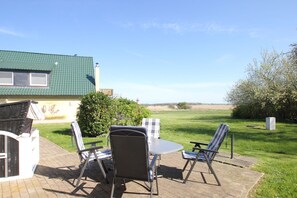An outdoor patio with a table and chairs, a brick pathway, and a view of a green field and distant landscape.