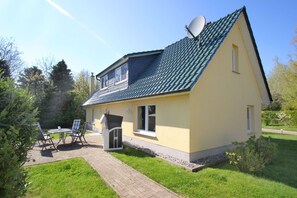 A single-story house with a satellite dish, a small patio with chairs, and a garden area. - Kormoran Vacation Home—near the water in a quiet location, with a private garden and terrace (Breege)