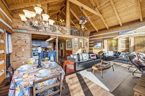 A spacious living area with a high ceiling, a dining table set for four, a leather sofa, and a balcony with a view. - Secluded Unobstructed Panoramic Mtn View w/ Dual Suites+Loft+ Game Room+Hot Tub (Gatlinburg)