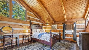 Un dormitorio tipo cabaña de troncos con una cama de madera, un escritorio y un ventanal con vistas a árboles.