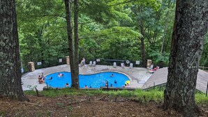 Una piscina rodeada de árboles, con algunas personas nadando y otras relajándose en el borde.