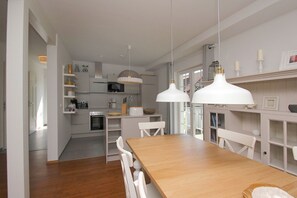 A modern kitchen with white cabinetry, a wooden dining table, and pendant lights. - Vacation home Freya - comfortable Swedish house close to the beach with sea view - (Wiek)