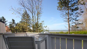 Une terrasse en bois avec une rambarde en métal, donnant sur une étendue d’eau et des arbres.