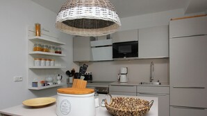 Une cuisine moderne avec des armoires blanches, un four à micro-ondes, une machine à café et un saladier en osier posé sur le comptoir.
