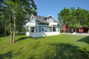 A two-story house with a porch, surrounded by a well-maintained lawn and trees. - Vacation home Freya - comfortable Swedish house close to the beach with sea view - (Wiek)