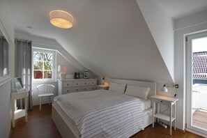 A bedroom with a sloped ceiling, a bed with striped bedding, a bedside table with a lamp, a chair, and a window with curtains. - Vacation home Freya - comfortable Swedish house close to the beach with sea view - (Wiek)