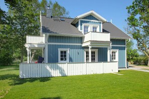 Ein zweigeschossiges Haus mit blauer Fassade und weißem Zierrahmen, einer überdachten Veranda und einem umzäunten Garten.