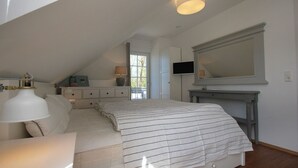 Une chambre à coucher comprenant un lit, une table de chevet, une lampe, une commode, un téléviseur et un grand miroir.