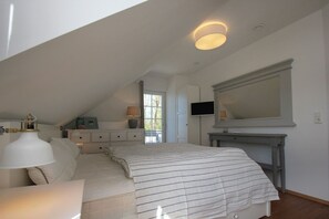 Un dormitorio con cama, mesita de noche, lámpara, cómoda, televisor y un espejo grande.