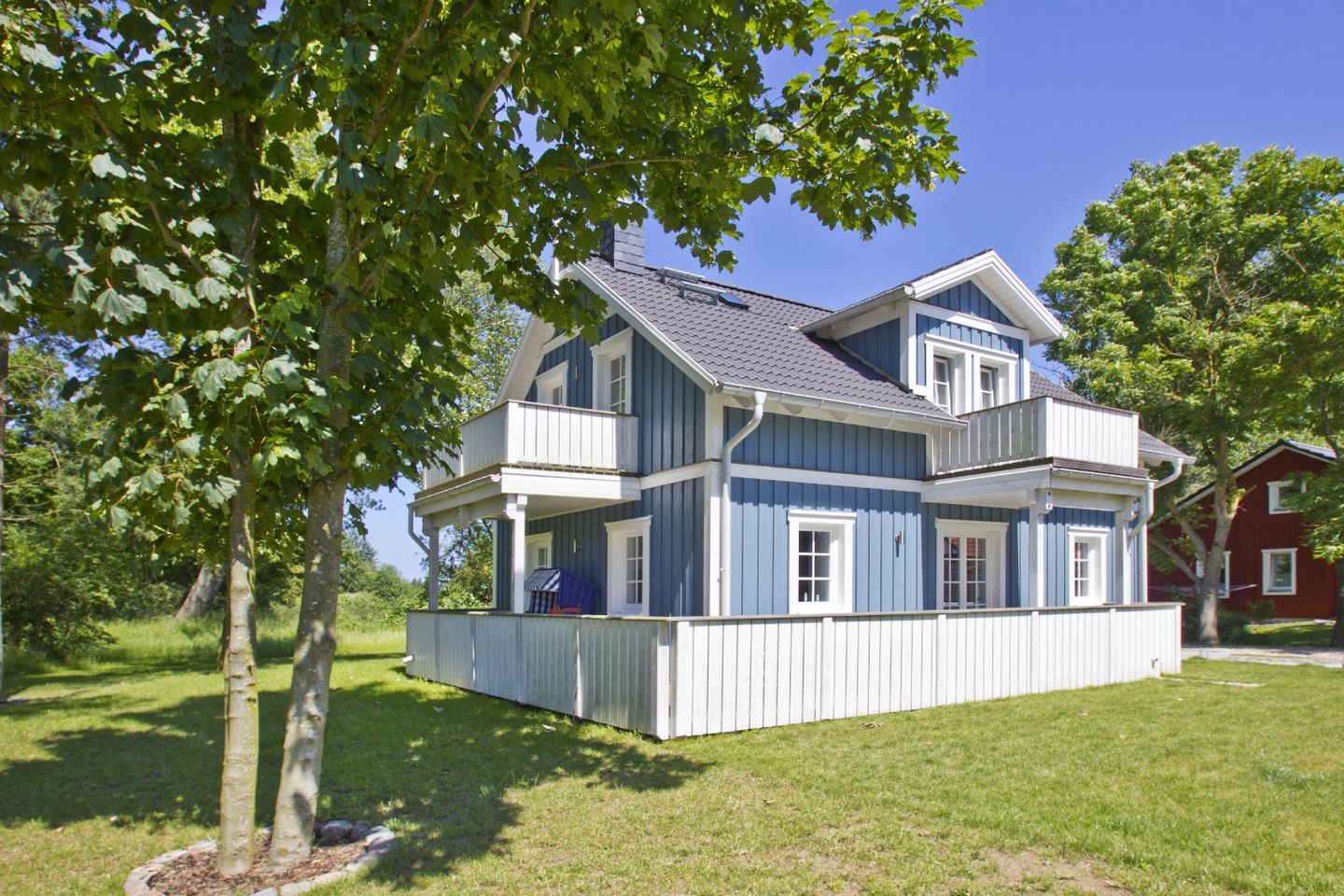 A two-story house with a balcony, surrounded by trees and a well-maintained lawn.