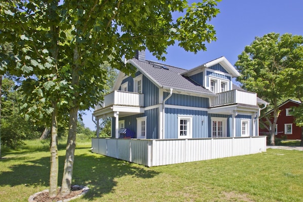 A two-story house with a balcony, surrounded by trees and a well-maintained lawn.