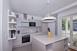 A modern kitchen with white cabinetry, a built-in oven, a microwave, and a hanging light fixture.