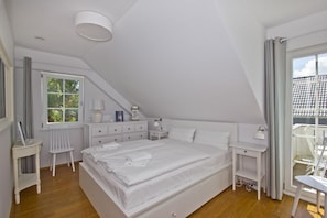 A bedroom with a large bed, a desk, a chair, and a window with curtains.