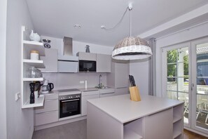 A modern kitchen with white cabinetry, a built-in oven, a microwave, and a hanging light fixture.
