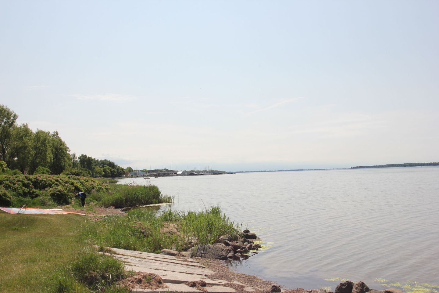 A calm lake with a grassy shore and a concrete path leading to the water.